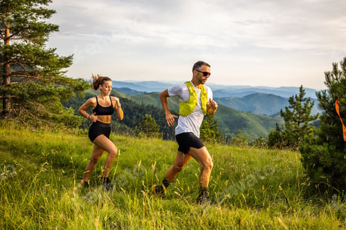 Preview: Caucasian couple running on a mountain trail with lush greenery in the early morning