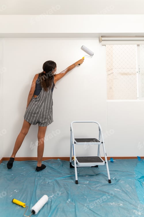 Preview: Woman using a roller to paint the wall at home