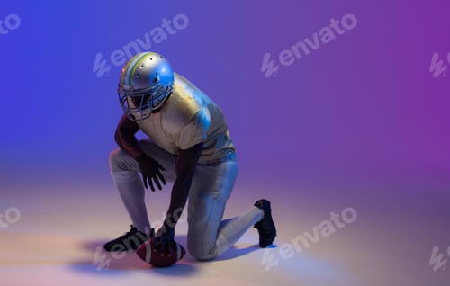 Preview: African american male american football player holding ball with neon blue lighting