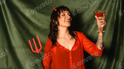 Preview: Portrait of a woman in a red dress with horns and trident holding red cocktail