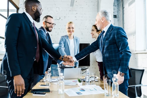 Preview: cheerful businesswomen putting hands together with multicultural coworkers