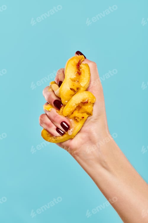 Preview: unknown female model squeezing juicy delicious persimmon in her hand on vibrant blue background
