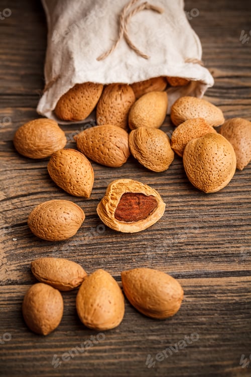 Almonds spilling from bag on rustic wooden surface