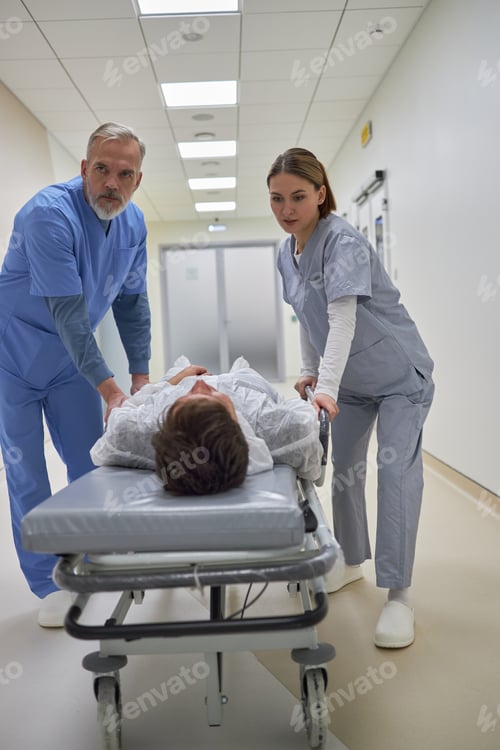 Preview: Middle Aged Man and Young Adult Woman Transporting Patient in Hospital
