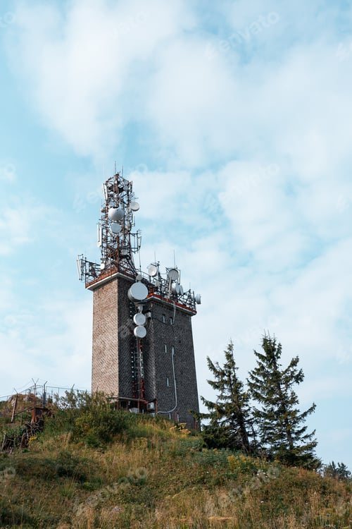 Preview: Low angle of a telecommunication tower and coniferous trees against the cloudy sky