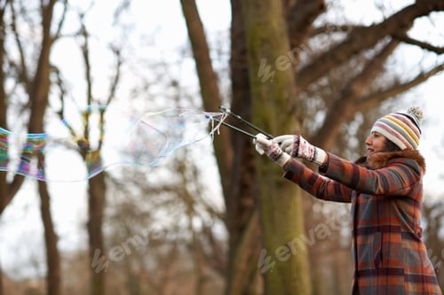 Preview: Woman in park using bubble wand to make bubbles