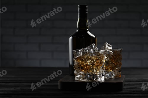 Preview: Whiskey with ice cubes in glasses and bottle on black wooden table, space for text