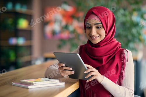 Preview: Cheerful muslim lady SMM-manager using digital tablet at cafe
