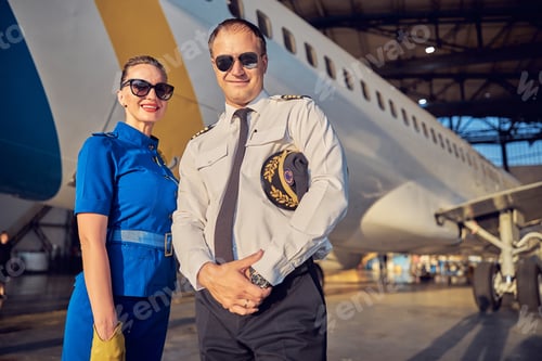 Preview: Smiling cheerful female air hostess with captain looking at the photo camera