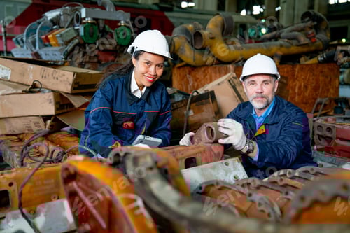 Preview: Factory worker man sit and touch metal machine part and stay with Asian factory woman