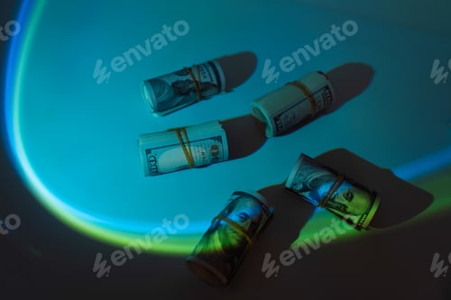 Preview: Tubes of hundred dollar bills rewound with a rubber band under blue light