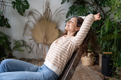 Preview: Dreamy woman relaxing in tropical resort-style garden at home, female gardener resting in greenhouse
