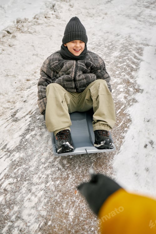 Preview: Smiling Caucasian Boy Sledding down Snowy Hill during Winter Outdoor Activity