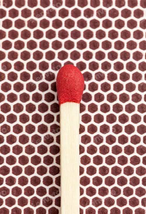 Preview: Macro photo of a single red-tipped wooden matchstick resting on the brown matchbox