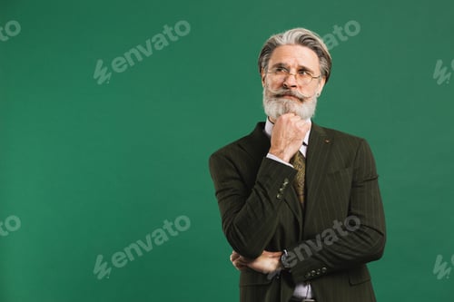 Preview: A bearded middle-aged teacher in khaki suit holding a beard and thinking on a green background
