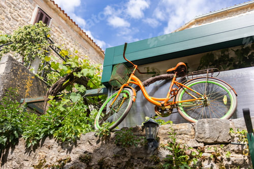 Preview: Vintage orange bicycle on stone wall with greenery. Creative outdoor decor