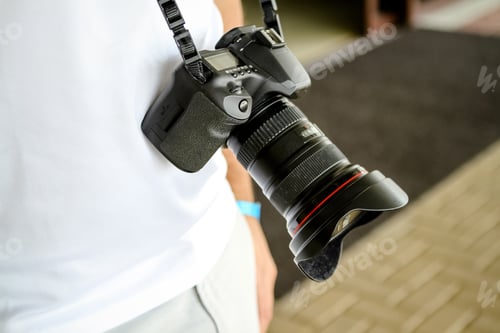 Preview: Câmera fotográfica no pescoço de um homem com roupa branca.
