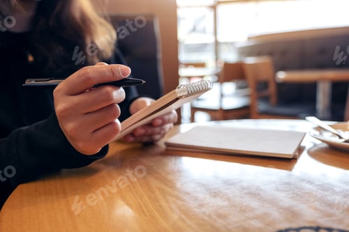 Preview: Closeup image of a woman holding and writing on blank notebook on table in cafe