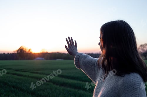 Preview: Silhouette of a woman at sunset in a field against the sky, rear view.