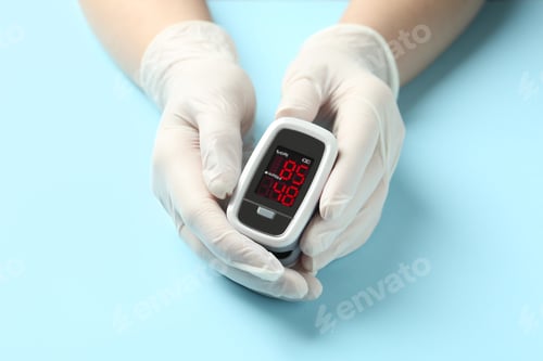 Preview: Doctor in gloves holding fingertip pulse oximeter at light blue background, closeup