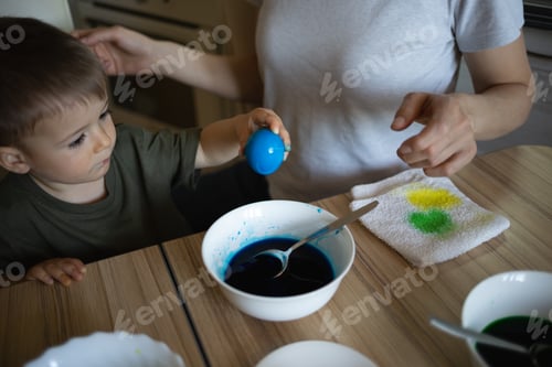 Preview: little cute boy paints eggs for easter sitting in the kitchen at the table