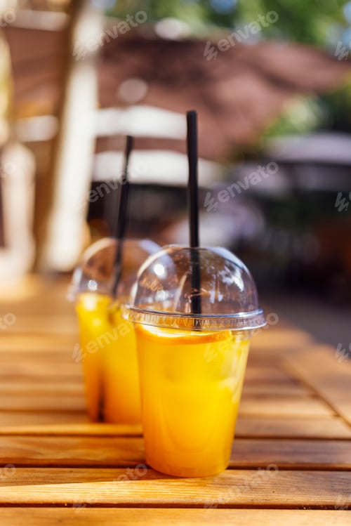 Preview: Two orange color cocktails in plastic glasses with straws against the backdrop of an open air cafe