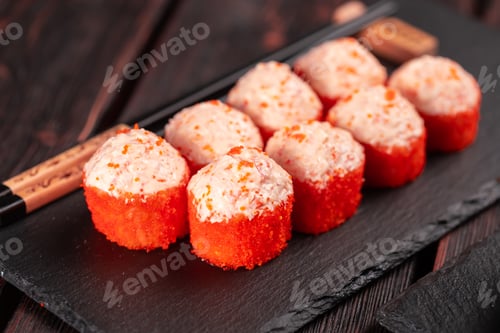 Preview: Sushi roll with mayonnaise sauce and red tobiko caviar served on black board and soy sauce.