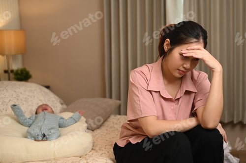 Preview: Exhausted young mother suffering from postnatal depression sitting next to her son on bed.