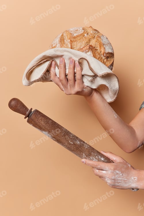 Preview: Vertical shot of unrecognizable female baker holds round loaf of freshly baked crusty bread on