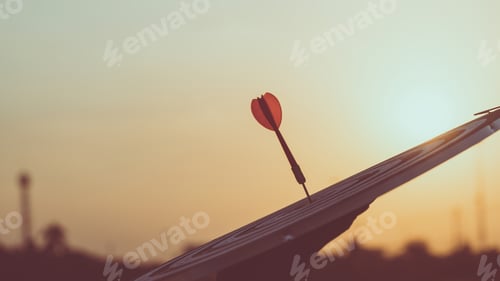 Preview: Close up red dart arrow hitting target center dartboard on sunset background.