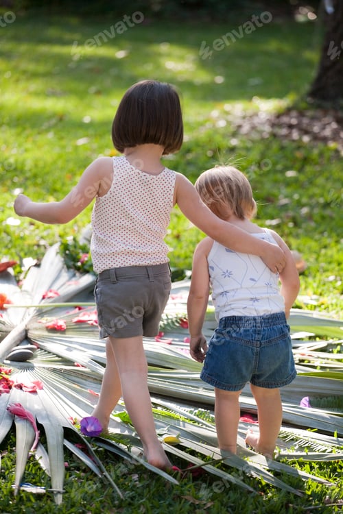 Preview: Girl with arm around toddler sister with flower and leaf display in garden