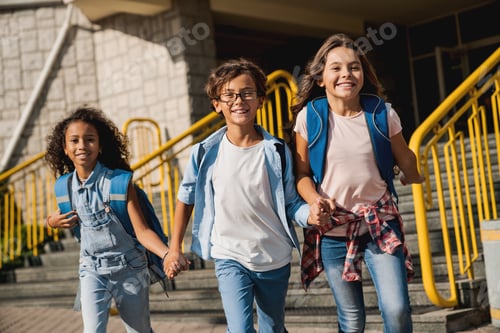 Preview: Happy kids with rucksacks walking holding hands at school yard