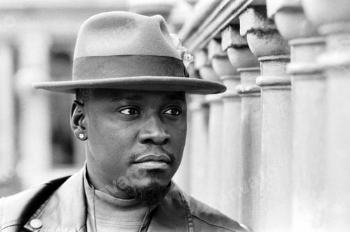 Preview: Serious portrait of black man with a hat beside columns in a black and white image.