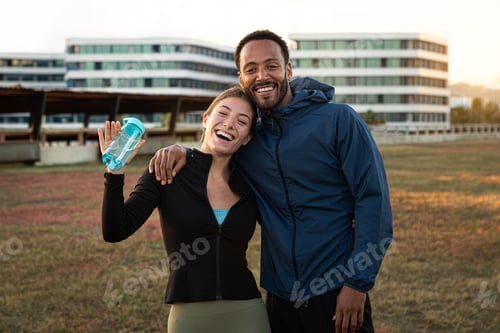 Preview: Young multiracial couple looking at camera smiling and waving hand after workout outdoors.