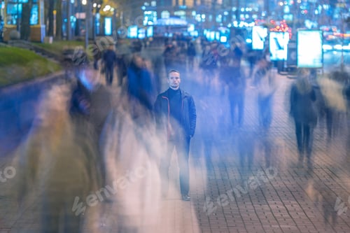 Vista previa: The man stand in the street with a stream of people. evening night time
