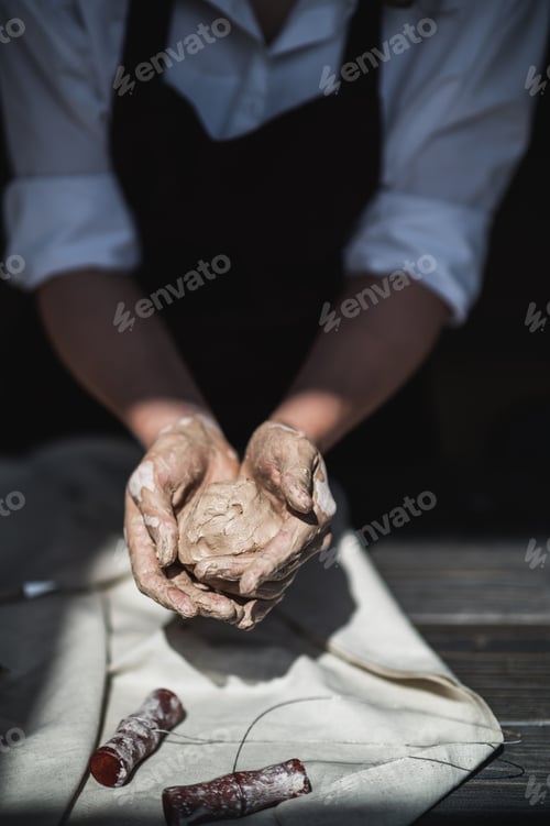 Preview: Wet hands covered with gray clay of potter holding raw piece of clay