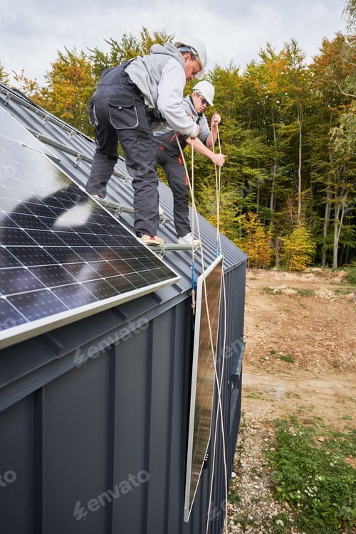Preview: Workers lifting up photovoltaic solar module while installing solar panel system on roof of house.