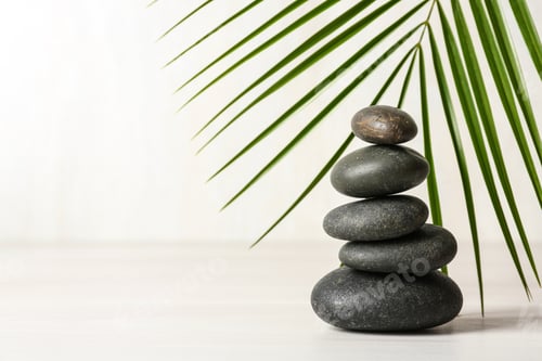 Preview: Stack of spa stones and palm leaf on table against white background, space for text