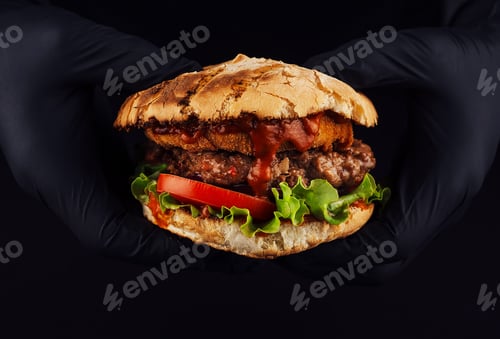 Preview: Man holds burger with nugget and cutlet in hands in black gloves