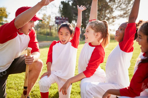 Preview: Girl baseball team kneeling with their coach, raising hands
