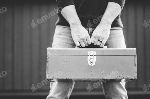 Preview: Grayscale shot of a technician holding a toolbox outdoors with a blurry background