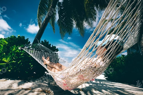 Preview: Woman relaxing in the shade of palms on a hammock.