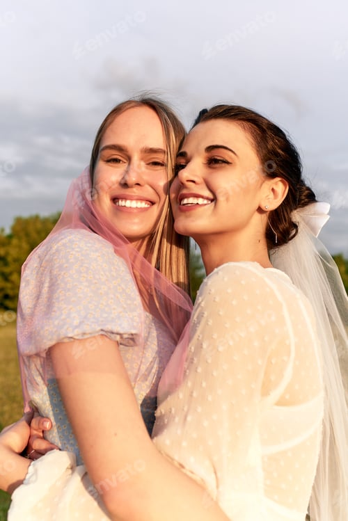 Preview: A happy charming bride in a white dress with a white veil and a bridesmaid with a pink veil gently