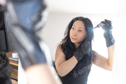 Preview: Closeup woman dyeing hair. Middle age Asian woman colouring dark hair with gray roots at home.