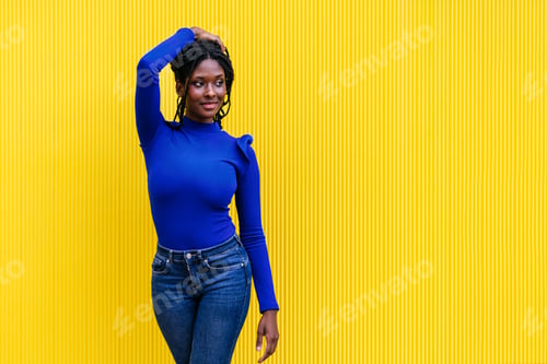 Preview: Radiant AfroAmerican Woman Smile, Posing by Yellow Wall, Touching Hair, Wearing Colorful Blue Attire