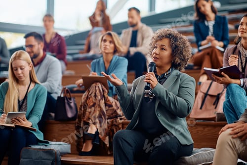 Preview: Mature businesswoman using microphone while speaking from audience during a seminar.