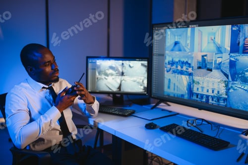 Preview: African-American security officer watching the screens talking on radio in control room
