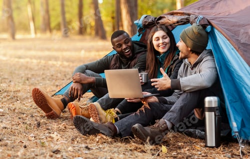 Preview: Cheerful friends discussing hiking route, using laptop