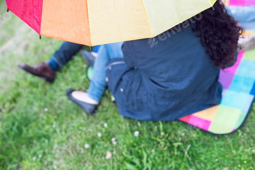 Preview: Low section of people sitting under colorful umbrella