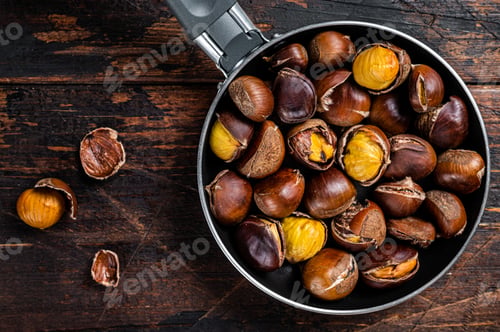 Preview: Roasted chestnuts nuts in a pan. Wooden background. Top view